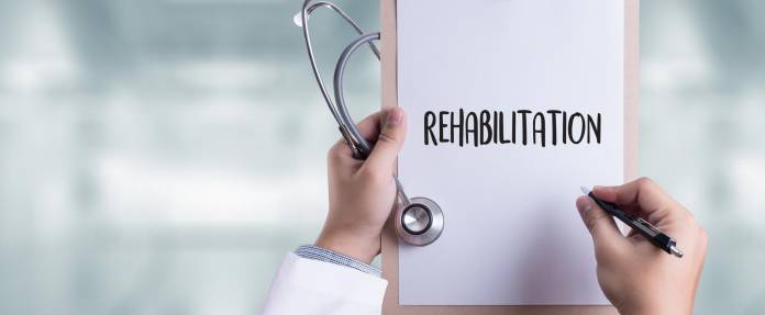 Das Wort Rehabilitation von einem Arzt auf einem Papier geschrieben, dass an einem Klemmbrett hängt