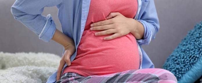 Schwangere Frauen fasst sich an Oberbauch und Rücken