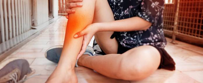 Junge Frau sitzt auf dem Boden und hält sich das Bein