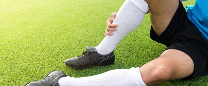 Fußballspieler sitzt auf dem Rasen und hält sich das rechte Schienbein