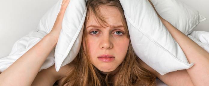 Müde Frau mit Kissen über dem Kopf