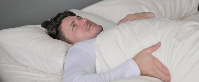 Mann - liegend im Bett - mit Schmerzen