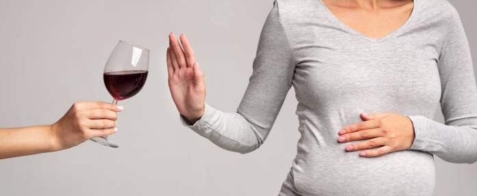 Schwangere Frau lehnt ein Glas Rotwein ab