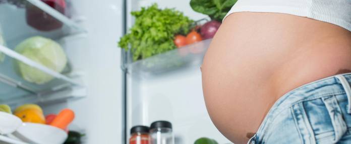 Schwangere Frau steht vor dem Kühlschrank