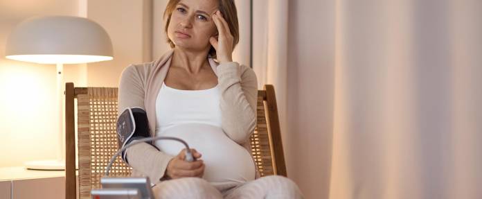 Schwangere Frau mit Kopfschmerzen und Blutdruckmessgerät am Arm