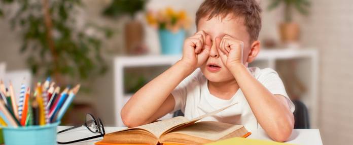 Junge reibt sich die Augen vom Lesen im Buch
