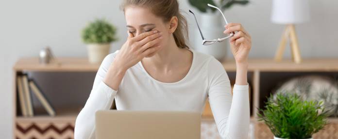 Junge Frau reibt sich die Augen am Arbeitsplatz
