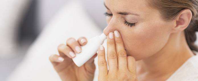 Frau nimmt Nasenspray gegen Schnupfen