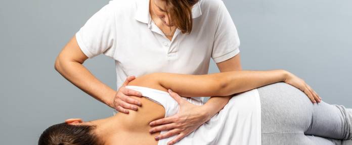 Frau wird von einer Osteopathin auf der Seite liegend am Rücken behandelt