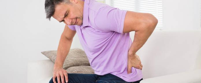 Mann sitzend auf dem Sofa leidet an Rückenschmerzen