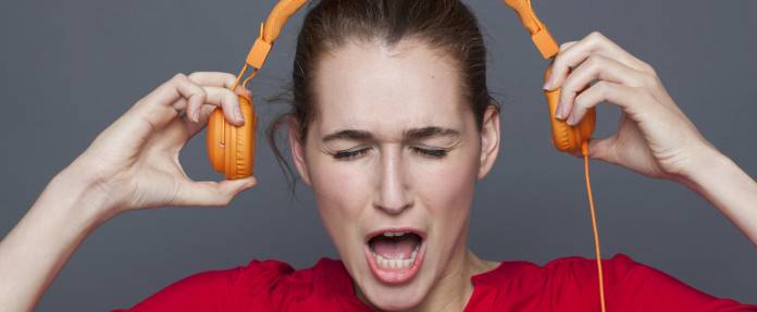Frau mit verzerrtem Gesicht setzt orangene Kopfhörer ab