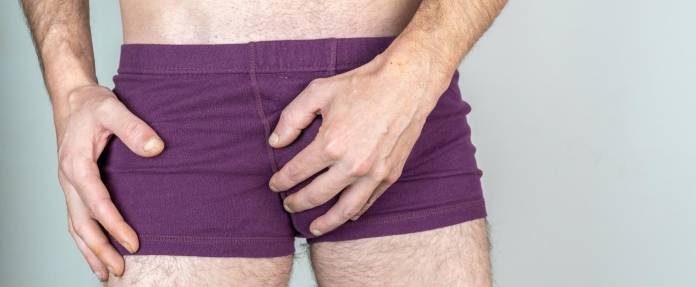 Mann fasst sich an die Unterhose