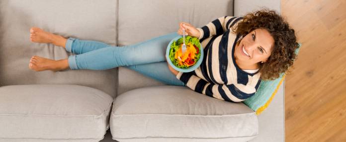 Frau essend mit einer Schüssel Salat auf dem Sofa