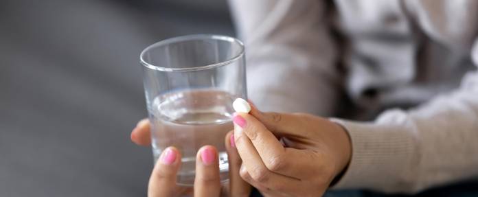 Frau mit Medikament und Wasserglas in der Hand