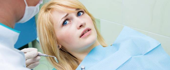 Junge blonde Frau liegend auf Behandlungsstuhl mit Angst vor dem Zahnarzt 