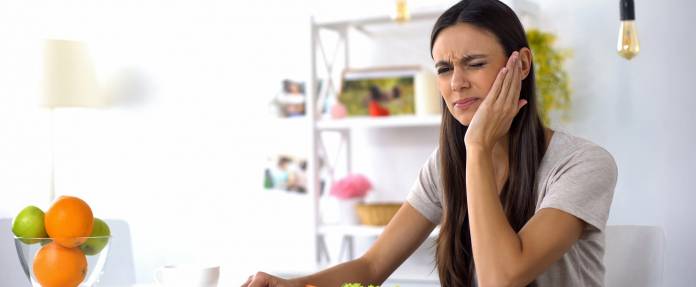 Junge Frau fasst sich schmerzhaft an die Wange während dem Essen