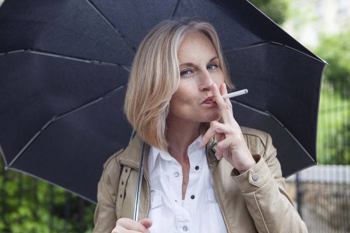 Frau mit Regenschirm in der Hand zieht an einer Zigarette